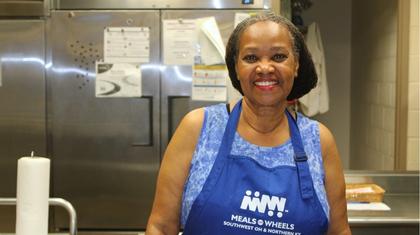 Woman in a kitchen wearing an apron that says Meals on Wheels of Southwest OH and Northern KY